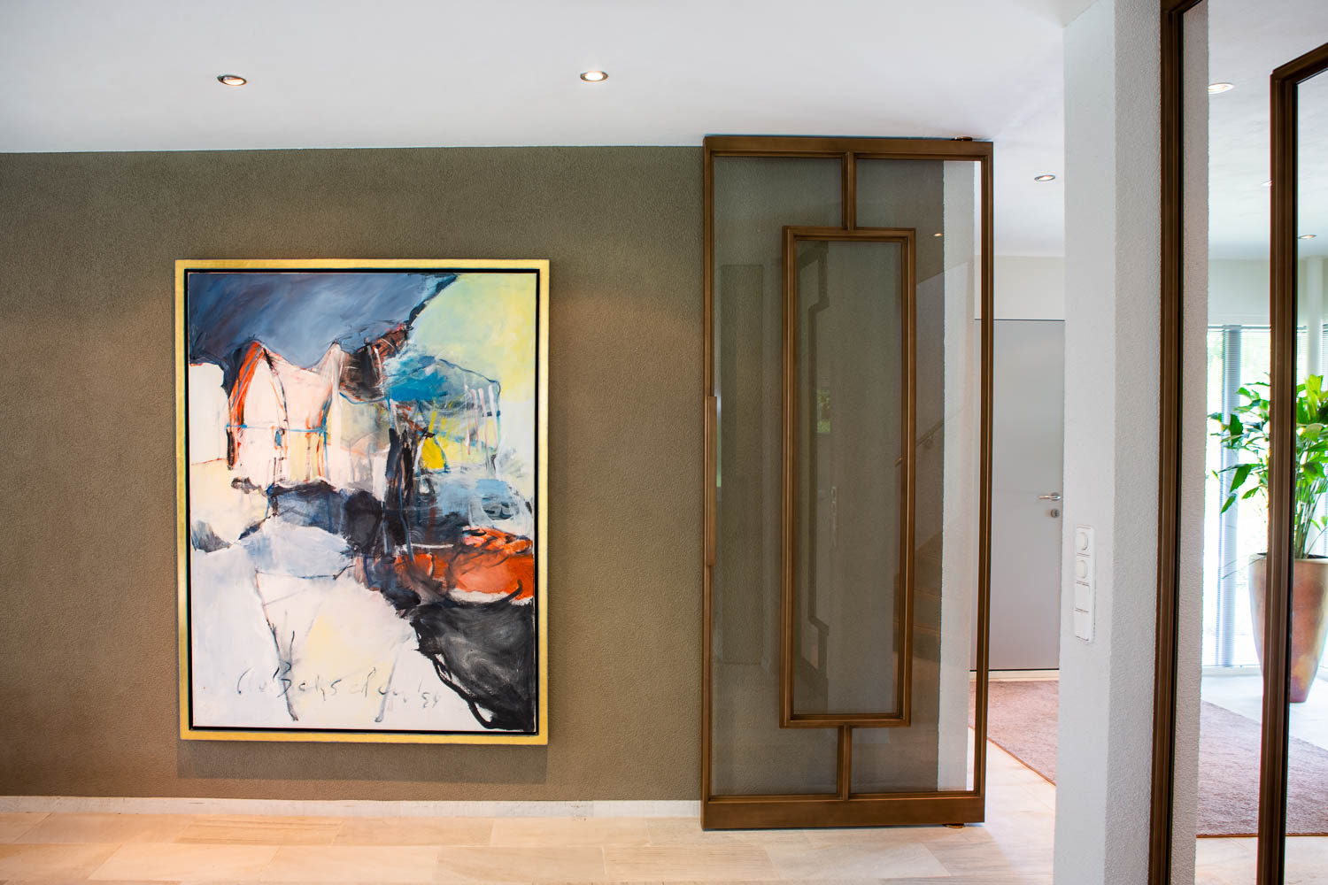 Moderne bronzen stalen binnendeur met glas, naast een groot kunstwerk in een stijlvol interieur.